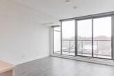 Located in Toronto's vibrant College Street neighbourhood, this well-appointed 2-bedroom, 2-bathroom unit offers a thoughtfully designed single-floor layout with modern finishes throughout. The open-concept kitchen anchors the living space, showcasing white cabinetry, quartz countertops, a large island with pendant lighting, stainless steel appliances including a French door refrigerator, electric range, built-in microwave, and dishwasher. Wide-plank hardwood flooring flows through the main living areas, and a glass sliding partition connects the kitchen to the living room, maximizing light and flexibility. The primary bedroom is a comfortable, well-proportioned room featuring black-framed windows that let in natural light, along with a generous built-in closet with sleek sliding doors and matte black hardware. The second bedroom similarly benefits from natural light and hardwood floors. Both bathrooms are finished in crisp white, with the main bath offering a soaker tub framed by white subway tile and tile flooring. The second bathroom features a white vanity with an integrated sink and a large mirror. A dedicated in-unit laundry room houses a stacked front-load washer and dryer. Recessed lighting and clean white walls throughout give the space a bright, contemporary feel.