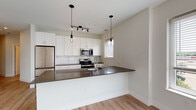 Located at 10 Willard Rd in Norwalk, Connecticut, this thoughtfully designed single-floor residence offers a clean, modern aesthetic throughout. Light-toned hardwood flooring flows seamlessly across every room, creating a cohesive and bright atmosphere.

The open-concept kitchen serves as the heart of the space, featuring crisp white shaker cabinetry, dark quartz countertops, a white subway tile backsplash, and a full suite of stainless steel appliances including a French door refrigerator, electric range, built-in microwave, and dishwasher. A peninsula with pendant lighting provides additional prep space and connects effortlessly to the adjacent living area. The living room is generously sized, bathed in natural light from a wide bank of windows that frame outdoor views.

A well-lit hallway connects the living spaces to the private areas, which include bedrooms with natural light from large windows and access to well-appointed bathrooms. One bathroom features a tub-shower combination with tiled surround, a white vanity, and dark countertop. A second bathroom includes accessibility-friendly grab bars, a walk-in shower area, and matching vanity finishes. Additional storage is offered through a walk-in closet with built-in shelving. Recessed lighting and modern fixtures complete the polished, contemporary feel of this residence.
