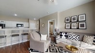This single-floor residential unit offers a thoughtfully arranged layout that balances comfort and functionality. The open-concept living area serves as the heart of the home, featuring warm neutral-toned walls, hardwood-style flooring, and a seamless connection to the kitchen. The living room provides generous space for seating and entertaining, with recessed lighting and a relaxed, modern ambiance.

The galley-style kitchen is designed for efficiency, featuring crisp white cabinetry extending to the ceiling, white countertops, a classic subway tile backsplash, and black appliances including a refrigerator, range, microwave, and dishwasher. A pantry closet and a breakfast bar with barstool seating add to the kitchen's practicality.

The unit includes two bedrooms, each finished with the same hardwood-style flooring and fitted with windows that allow natural light to filter in. Both rooms offer space for a bed and a workspace or additional furnishings.

Two full bathrooms serve the unit, each appointed with white vanity cabinetry, white countertops, large mirrors, and shower-tub combinations with curtains. The consistent neutral color palette and clean finishes throughout the bathrooms create a cohesive and tidy feel. The overall design of this unit emphasizes a modern, neutral aesthetic with functional spaces suited to everyday living.