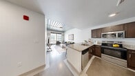 Located at 1 Merrimack Plaza in Lowell, MA, this two-bedroom, two-bathroom residence offers a thoughtfully designed open-concept layout. The living room is a standout space, featuring distinctive exposed metal ceiling panels that lend an industrial-modern aesthetic, polished concrete floors, and large windows that allow generous natural light and views of the surrounding streetscape. The kitchen flows seamlessly from the living area and is equipped with dark espresso cabinetry, granite countertops, stainless steel appliances including a range, microwave, dishwasher, and refrigerator, and a peninsula with seating that doubles as a casual dining space. Both bathrooms are finished with matching dark cabinetry, granite-topped vanities, and wood-style flooring; one bathroom features a walk-in shower. The primary bedroom is a comfortable and well-lit retreat with carpeted flooring and a large window overlooking the exterior. The second bedroom provides a versatile space suitable for use as a guest room or home office, also with carpeted flooring. Throughout the residence, clean white walls and consistent finishes create a cohesive, contemporary atmosphere well-suited for urban living in downtown Lowell.