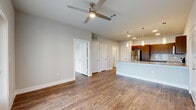This well-appointed one-bedroom, one-bathroom residence in San Antonio, TX offers a thoughtfully designed single-floor layout with an open-concept living and kitchen area. Rich wood-look flooring flows throughout, complementing the neutral gray tones of the walls and crisp white trim. The kitchen is a standout feature, equipped with stainless steel appliances including a refrigerator, range, and microwave, dark-stained wood cabinetry, a white tile backsplash, and a granite-topped island with pendant lighting above — ideal for both cooking and casual dining. The open living area benefits from ceiling fan ventilation and connects seamlessly to a private patio via French doors, bringing in natural light and outdoor views. The spacious primary bedroom accommodates a comfortable retreat, featuring a ceiling fan, a natural light-filled window, and access to a closet alongside an in-unit stacked washer and dryer. The bathroom is finished with wood-look flooring, a glass-enclosed walk-in tile shower, and clean, modern fixtures. Additional storage is provided through three closets and a pantry, rounding out the practical and functional design of this San Antonio residence.