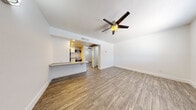 This single-floor unit offers a clean, modern interior with a thoughtfully arranged open layout. The main living area is finished with wood-look plank flooring and features a ceiling fan with a light fixture, creating a comfortable and well-ventilated space. Large windows with blinds allow natural light to fill the room, contributing to an airy and welcoming ambiance. The entry door is conveniently located within the living space, providing direct access to the unit.

The kitchen is semi-open to the living area and separated by a breakfast bar with granite-style countertops, ideal for casual dining or food preparation. White cabinetry lines the kitchen walls, complemented by stainless steel appliances including a full-size refrigerator, a gas range, a built-in microwave, and a single-basin sink. Recessed lighting and warm-toned walls give the kitchen a distinct and inviting character, while tile flooring provides a practical surface in this area.

The bathroom is well-appointed with a wide vanity featuring a granite-style countertop, white cabinetry below, a large mirror, a toilet, and a full bathtub with a shower. Light tile flooring ties the space together with a clean, neutral finish. Overall, this unit presents a cohesive and functional living environment with updated finishes throughout.