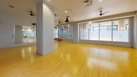 Located at 214 E Grace St in downtown Richmond, Virginia, this single-floor fitness and movement studio is designed to support a wide range of group exercise, wellness, and instructional activities. The space is defined by its warm, polished hardwood flooring that spans the entire open floor plan, providing a clean and durable surface well-suited for yoga, dance, pilates, or general fitness classes.

The studio features a ceiling-mounted projector paired with a wall-mounted projection screen, enabling instructors to display visual content during classes or presentations. Multiple ceiling fans are distributed throughout the space, ensuring consistent air circulation during active sessions. Recessed lighting complements the natural light that filters in through large frosted-glass windows along one wall, creating a bright yet diffused atmosphere conducive to focused movement and exercise.

Full-length mirrors along one wall expand the sense of space while allowing participants to monitor their form and technique. A built-in shelving unit offers convenient storage for equipment and personal items. The neutral gray and white color palette throughout the walls and ceiling contributes to a calm, professional ambiance. The open layout provides ample room for group classes while maintaining flexibility for various configurations and uses.