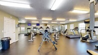 Located at 800 East Spring Street in Cookeville, Tennessee, this dedicated fitness center offers a generously sized, single-floor exercise room designed to support a comprehensive workout experience. The space features a durable dark rubber flooring throughout, providing a safe and practical surface for a wide range of physical activities.

The exercise room is well-stocked with an extensive selection of cardio equipment, including multiple treadmills, elliptical trainers, and stationary bikes — both upright and recumbent — catering to varying fitness levels and preferences. Strength training needs are addressed with a multi-function cable machine, a weight bench, and free weights. Wall-mounted mirrors along one side of the room enhance the sense of space and allow users to monitor their form during workouts.

Multiple flat-screen TVs are mounted on the walls, providing entertainment during exercise sessions. Natural light filters in through several windows fitted with blinds, complementing the bright overhead fluorescent lighting that illuminates the entire floor. The textured ceiling adds a classic architectural touch to the interior.

A restroom is conveniently located within the facility, along with an AED unit and waste receptacles, reflecting a commitment to safety and user comfort. The open, uncluttered layout ensures ample room to move freely between equipment stations, making this fitness center a functional and well-appointed amenity.
