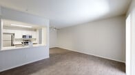 This single-story space is designed with a clean, modern aesthetic and a neutral color palette of soft whites and warm grays. The open-concept living area is a central highlight, featuring wood-look plank flooring and a ceiling fan overhead. A pass-through counter connects the living area to the kitchen, which is outfitted with white cabinetry, stainless steel appliances including a built-in microwave, and recessed lighting, creating a bright and functional workspace.

A sliding glass door in one section of the living space introduces natural light and provides access to an outdoor area, further enhancing the open feel of the interior. The layout, as revealed by the floor plan, includes multiple rooms connected by a hallway. One bedroom features soft carpeting, a sliding-door closet with built-in shelving, and a window with an exterior view. Another room includes wood-look flooring and a ceiling fan, offering flexibility in use.

The bathroom is finished with a quartz-topped vanity, undermount sink, brushed nickel fixtures, a large mirror with overhead lighting, and a tub-shower combination. Throughout the space, clean white doors, crisp baseboards, and consistent flooring choices contribute to a cohesive and functional living environment.