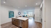 Located at 377 E Main St in Branford, CT, this single-floor unit offers a thoughtfully designed open-concept layout with modern finishes throughout. The kitchen serves as a central hub, featuring a large island with a white quartz countertop, an undermount sink, bar seating, dark wood cabinetry, and stainless steel appliances including a refrigerator, range, microwave, and dishwasher. The kitchen flows seamlessly into the living area, which is bright and airy, benefiting from natural light through large windows that overlook the surrounding neighborhood. Wood-style flooring runs consistently throughout the main living spaces, adding warmth to the clean, contemporary aesthetic defined by white walls and recessed lighting. The primary bedroom includes a wall-mounted climate control unit, a large window, and access to a generously sized walk-in closet outfitted with wire shelving and wood flooring. A second bedroom also offers natural light and ample space. The full bathroom features large-format tile flooring, a wood-toned vanity with a white countertop, and a glass-enclosed tub and shower combination. A dedicated in-unit laundry area with a full-size washer and dryer completes this well-appointed space.