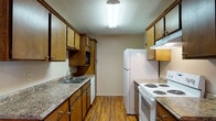 This single-floor residence offers a well-organized layout with distinct living, dining, kitchen, bedroom, and bathroom areas. The galley-style kitchen is efficiently designed with warm wood cabinetry lining both sides, granite-look countertops, and a full suite of white appliances including an electric range, refrigerator, dishwasher, and built-in microwave. A double-basin sink and ample upper and lower cabinet storage complete the functional workspace, all finished with durable wood-look flooring. Adjacent to the kitchen, a dedicated dining area is illuminated by a pendant light and flows seamlessly into the main living space, where wood-look flooring continues underfoot. The living room features a ceiling fan with light fixture and connects directly to the front entry door, creating an open and welcoming atmosphere. The bedroom is generously sized, featuring plush wall-to-wall carpet, a ceiling fan, and a window that brings in natural light. The full bathroom is finished with wood-look flooring, a single-sink vanity with dark wood cabinetry and a wide mirror, and a full shower-tub combination. The neutral color palette and consistent finishes throughout create a cohesive and comfortable living environment.