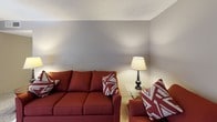 This single-story Magnolia unit offers two bedrooms and two bathrooms across a practical, well-organized layout. The living area features carpet flooring and neutral gray walls, providing a versatile backdrop for furnishings. Two sofas fit comfortably within the space, making it well-suited for relaxing or entertaining.

The kitchen is outfitted with dark cabinetry, stone-look countertops, stainless steel appliances including a refrigerator and dishwasher, and dark wood-style flooring that extends throughout the wet areas of the unit. Ample upper cabinet storage supports everyday functionality.

The primary bedroom is generously sized with carpet flooring, windows that allow natural light, and a mirrored sliding closet that enhances the sense of space. The second bedroom, also carpeted, features a window with exterior views and dedicated dresser storage. Both rooms share a warm, understated aesthetic with taupe-toned walls and textured ceilings.

The two bathrooms each feature dark wood-style flooring and white fixtures. One includes a standalone walk-in shower with a glass door, while the second offers a full tub-shower combination with stone-look countertops at the vanity, providing practical storage and prep space.