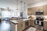 This thoughtfully designed one-bedroom, one-bathroom residence at Everleigh Duluth offers a seamless open-concept layout connecting the kitchen, dining, and living areas. The kitchen serves as a central highlight, featuring warm wood-tone cabinetry, quartz countertops, a herringbone tile backsplash, stainless steel appliances including a French door refrigerator, a deep undermount sink, and elegant pendant lighting that anchors the space. Durable wood-style flooring flows throughout the main living areas, adding warmth and continuity.

The living room is bright and inviting, benefiting from large windows dressed with sheer curtains and blinds that allow generous natural light. A ceiling fan adds comfort, while the open sightlines create an airy, spacious feel.

The bedroom is a calm retreat, carpeted for comfort and illuminated by a large window. It offers ample space for a full bedroom suite and provides access to a well-organized walk-in closet.

The bathroom is spa-inspired, showcasing a quartz-topped vanity with wood cabinetry, a large framed mirror, and a glass-enclosed walk-in shower. The walk-in closet is directly accessible from the bathroom, offering convenient and practical storage.

The entryway features smooth wood-style flooring and clean lines, providing a welcoming transition into the home. Every detail reflects a refined, contemporary aesthetic suited for comfortable everyday living.