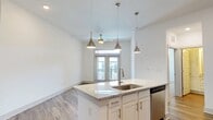 Located at 4454 Tropea Way in Jacksonville, Florida, this single-floor residence offers a clean, modern aesthetic throughout. The open-concept kitchen serves as the heart of the home, anchored by a large island with granite countertops, an undermount sink, and stylish pendant lighting overhead. White shaker cabinetry, a subway tile backsplash, and stainless steel appliances — including a refrigerator, range, microwave, and dishwasher — complete the well-appointed kitchen. Hardwood-style flooring flows through the main living areas, adding warmth and continuity to the space. The living area is bright and open, leading to French doors with transom windows that open to a private balcony, allowing natural light to fill the room. A ceiling fan provides additional comfort. The bedrooms feature plush carpeting, ceiling fans, and windows that bring in natural light. The primary suite includes a spacious walk-in closet with wire shelving. The bathroom is finished with granite countertops, white cabinetry, a tiled walk-in shower, and hardwood-style flooring, maintaining the home's consistent, contemporary style throughout.