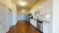 This well-appointed single-floor unit offers a thoughtfully designed layout that balances modern finishes with everyday functionality. The kitchen serves as a standout feature, showcasing crisp white cabinetry with brushed nickel hardware, granite countertops, a classic white subway tile backsplash with under-cabinet lighting, and a full suite of stainless steel appliances including a refrigerator, range, over-the-range microwave, and dishwasher. Rich, dark hardwood flooring runs throughout the main living and kitchen areas, adding warmth and contrast to the bright, neutral color palette.

The living area is generously sized and benefits from large floor-to-ceiling windows and sliding glass doors that flood the space with natural light and offer expansive views of the surrounding cityscape. A ceiling fan adds comfort to the room.

The bedrooms are carpeted for comfort and feature large windows with horizontal blinds, providing sweeping panoramic views of the surrounding area. Corner windows in one bedroom maximize the sense of openness and light.

The bathroom is finished with the same attention to detail found throughout the unit, featuring granite countertops, white cabinetry, wood-look flooring, a large mirror, and a subway-tiled bathtub and shower surround — all presented in a clean, modern aesthetic.