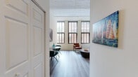 This 2-bedroom, 1-bathroom residence in Baltimore, MD blends industrial character with modern comfort. The living room is a standout space, featuring soaring ceilings with whitewashed exposed brick, oversized multi-pane windows that flood the room with natural light, and rich hardwood-style flooring. The open layout connects seamlessly to a dining area, creating an inviting, loft-inspired atmosphere.

The galley-style kitchen is well-appointed with dark espresso cabinetry, granite-look countertops, and a full suite of stainless steel appliances, including a refrigerator, electric range, and built-in microwave. A bifold-door pantry provides additional storage.

The primary bedroom continues the loft aesthetic with whitewashed brick ceilings and large windows, while the second bedroom offers a cozy, well-lit retreat with its own window. A spacious walk-in closet with wire shelving systems provides generous storage. The bathroom includes a glass-enclosed shower stall, a single-sink vanity with dark cabinetry, and a large mirror.

A dedicated laundry area houses a stacked washer and dryer unit alongside a water heater. Hallways connect the rooms efficiently throughout the single-floor layout, completing this thoughtfully designed urban residence.