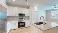 This thoughtfully designed single-floor unit offers a clean, modern aesthetic with cohesive finishes across every room. Light hardwood flooring runs throughout, complementing the bright, neutral color palette that creates an open and airy atmosphere.

The kitchen serves as the focal point of the living space, showcasing white shaker-style cabinetry, granite countertops with subtle speckled detailing, and a suite of stainless steel appliances including a range, over-the-range microwave, refrigerator with ice and water dispenser, and dishwasher. A central island with an undermount sink and gooseneck faucet provides both prep space and a natural gathering point. A stacked washer and dryer unit is conveniently integrated into the kitchen area, adding practical functionality. Open shelving offers additional storage nearby.

The bedroom is a calm, neutral retreat with a ceiling fan, a window with blinds that invites natural light, and direct access to a walk-in closet equipped with wire shelving for organized storage.

The bathroom features a granite-topped vanity with white cabinetry, an undermount sink, and a tiled walk-in shower with a sleek glass enclosure and marble-style surround. Additional overhead cabinet storage keeps essentials neatly tucked away. Recessed lighting throughout the unit enhances the clean, contemporary feel of this well-finished space.