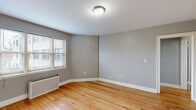 Located at 229-245 Parkside Ave in Buffalo, NY, this one-bedroom, one-bathroom unit offers a practical and well-organized single-floor layout. Warm hardwood floors run throughout the entire space, lending a consistent, classic character to every room. The living room is bright and open, featuring a radiator heating unit and natural light from double-hung windows with blinds. An adjacent dining area flows naturally from the living space, creating a connected and functional common area. The bedroom is a comfortable size, featuring two windows that invite ample natural light and a traditional cast-iron radiator. Four closets distributed throughout the unit provide generous storage. The kitchen is efficiently designed with white cabinetry, dark granite-style countertops, black appliances including an electric range and refrigerator, hardwood flooring, and a window for natural light and ventilation. The bathroom retains a classic aesthetic with white subway-style wall tiling accented by a bold black border, a full soaking tub, and a frosted window. Neutral gray walls throughout the unit create a clean, cohesive backdrop. A dedicated hallway connects the rooms, adding to the overall sense of organized flow within this well-maintained Buffalo residence.