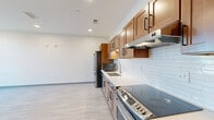 This single-floor unit is designed with a clean, modern aesthetic evident in every room. The kitchen serves as a central highlight, featuring warm medium-toned wood cabinetry with black hardware, light-colored countertops, and a white subway tile backsplash. A full suite of stainless steel appliances — including a refrigerator, range, dishwasher, and built-in microwave — lines the galley-style layout, complemented by light wood-look flooring that extends throughout the unit. Recessed lighting and under-cabinet illumination keep the space bright and functional.

The open area adjacent to the kitchen provides generous room for living or dining arrangements, maintaining the same light flooring and crisp white walls for a cohesive look. The bedroom is well-proportioned, featuring two windows with blinds that allow natural light to fill the room, creating an airy and comfortable atmosphere.

The bathroom is thoughtfully designed with accessibility in mind, incorporating grab bars, an open roll-in shower with white tile surround, and a wood-toned vanity with a white countertop and undermount sink. Light tile flooring and neutral walls complete the clean, functional design. Overall, the unit offers a bright, contemporary environment with consistent finishes throughout.