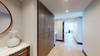Located in the heart of downtown Dallas, this single-floor high-rise unit at 1401 Elm St offers a sleek, contemporary design with an open, flowing layout. Light hardwood flooring runs throughout the main living areas, complementing the clean white walls and modern architectural details.

The living area is anchored by a wall-mounted television and a large corner window that frames sweeping panoramic views of the Dallas skyline, flooding the space with natural light. Adjacent to the living area, a dedicated nook with additional windows provides an ideal reading or lounge area, further showcasing the elevated city vistas.

The dining area is defined by an expansive floor-to-ceiling glass window wall, offering unobstructed views of the downtown skyline and filling the space with abundant sunlight throughout the day.

The kitchen features rich, dark wood cabinetry extending to the ceiling, stainless steel appliances, and a generous island topped with a striking marble-veined quartz countertop, accompanied by acrylic barstools.

The hallway is lined with full-height built-in storage cabinetry in a warm wood finish. Two bathrooms serve the unit: a secondary bath with warm tile flooring and a tub-shower combination, and a primary bath with a glass-enclosed shower, soaking tub, double vanity, and a large framed mirror.