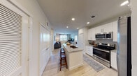 This single-floor residence is designed with a clean, contemporary aesthetic that emphasizes functionality and comfort. The open-concept layout connects the kitchen and living area seamlessly, creating a cohesive and spacious feel. The kitchen is a standout feature, equipped with white shaker-style cabinetry, granite countertops, stainless steel appliances—including a range, microwave, and French door refrigerator—and a central island with a built-in sink and bar seating, ideal for casual dining or entertaining. Recessed lighting illuminates the kitchen and flows into the living area, which features a ceiling fan, large windows with horizontal blinds, and light wood-style flooring that extends throughout the unit.

The living room is bright and welcoming, with natural light filtering through wide windows. Two bedrooms offer comfortable retreats, each featuring ceiling fans, windows with natural light, and access to well-designed closet space. The bathrooms mirror the kitchen's refined finishes, showcasing granite-topped white vanities with ample cabinetry and hardwood-style flooring. The primary bathroom includes a walk-in closet with built-in shelving, adding notable storage capacity. Overall, the unit presents a cohesive, modern design with consistent finishes throughout.