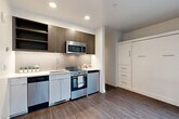 Located at 2369 Franklin Ave E in Seattle's Capitol Hill neighborhood, this efficiently designed studio unit offers a thoughtful layout that maximizes every square foot. The open main area features warm wood-tone laminate flooring and recessed lighting throughout, creating a clean, contemporary atmosphere.

The kitchen is well-appointed with stainless steel appliances, including a range with oven, over-the-range microwave, dishwasher, and compact refrigerator. Dark wood-grain upper cabinetry with open shelving contrasts beautifully against the white quartz countertops and subway tile backsplash. A built-in Murphy bed and storage cabinet system integrates seamlessly into the living area, optimizing the use of space without sacrificing style.

The hallway connects the main living space to the bathroom and features a stacked in-unit washer and dryer, along with additional built-in storage. A large window and sliding glass door at the end of the hallway flood the unit with natural light and provide direct access to a private patio enclosed by warm wood slatted fencing — a rare outdoor amenity that extends the living space outdoors.

The bathroom is finished in a crisp, all-white palette with a single-sink vanity, ample cabinet storage, and a full tub-shower combination, all accented by wood-look flooring for a cohesive, modern feel.
