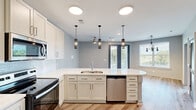 Located on Modern Ave in Hot Springs, AR, this thoughtfully designed single-story residence offers a streamlined, contemporary living experience across a well-utilized floor plan. The open-concept kitchen serves as the centerpiece of the home, showcasing white shaker cabinetry, quartz countertops, a large curved island with a stainless steel undermount sink, and stylish pendant lighting. Stainless steel appliances — including a French door refrigerator with ice maker, electric range, over-the-range microwave, and dishwasher — complete the kitchen. Decorative lattice cabinet accents and a subway tile backsplash add visual interest. Light wood-look flooring flows throughout the entire residence, creating a cohesive, modern aesthetic. The bedroom is a comfortable retreat, featuring a ceiling fan, a large window that invites natural light and outdoor views, and direct access to the bathroom. The bathroom offers a wide vanity with white cabinetry, quartz countertop, and a large mirror with contemporary lighting. A dedicated laundry room provides full-size side-by-side washer and dryer units with overhead shelving. The overall design balances functionality and modern style with a neutral, light-toned palette throughout.