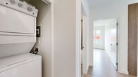 Located at 3046 Merchant Way in Langford, BC, this thoughtfully designed 2-bedroom, 2-bathroom unit offers a clean, modern aesthetic throughout. Light wood-toned flooring flows consistently across the open-plan living and kitchen areas, contributing to a bright and cohesive feel. Large windows in the living room flood the space with natural light and frame views of the surrounding Langford streetscape and neighbouring developments, creating an airy atmosphere despite the compact footprint.

The kitchen is well-appointed with two-tone cabinetry — white lower cabinets paired with warm wood-finish uppers — complemented by a white tile backsplash, stainless steel appliances including a full-size refrigerator and dishwasher, and a window above the sink for added ventilation and light.

Both bedrooms are bright and functional, each featuring large windows with neighbourhood views and baseboard heating. The primary bedroom offers a comfortable layout with a dedicated bathroom featuring a glass-enclosed shower stall, warm wood vanity cabinetry, and tile flooring. The second bathroom includes a full soaker tub and shower combination with neutral tile surround. A conveniently located in-unit stacked washer and dryer rounds out the practical amenities this well-designed residence has to offer.