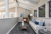 Located in Vestavia Hills, Alabama, this two-story space at 2944 Columbiana Court offers a distinctive architectural character defined by dramatic vaulted ceilings with exposed white-painted wood beams throughout. The design blends open, airy volumes with functional, well-appointed rooms across both levels.

The lower level is anchored by a spacious fitness area that commands attention with soaring double-height ceilings, floor-to-ceiling windows on multiple walls, and an abundance of natural light framing wooded outdoor views. A painted brick fireplace with a mounted television serves as a striking focal point, while hardwood-style flooring runs throughout. Cardio equipment and stationary bikes are thoughtfully arranged, and a spiral staircase elegantly connects the two floors. A casual seating area with bar-height furniture provides a relaxed gathering spot nearby.

The upper level features a generous open hallway with vaulted beamed ceilings, patterned carpet tile flooring, and a railed overlook. Multiple rooms branch off this corridor, including a conference room equipped with a wall-mounted display and a standing-height meeting table with seating, and a quiet nook highlighted by large windows and angled ceilings. The overall ambiance throughout is calm, modern, and professionally appointed.