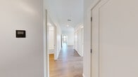 This well-appointed 2-bedroom, 2-bathroom unit is thoughtfully designed with a modern aesthetic and efficient single-floor layout. Light-toned hardwood flooring flows consistently throughout the space, complementing the clean white walls and crisp trim work that define each room.

The open-concept kitchen and living area serves as the heart of the unit. The kitchen is outfitted with white flat-panel cabinetry, a large waterfall-edge island with an integrated sink, stainless steel appliances including a refrigerator, electric range, and over-range microwave, and recessed lighting accented by pendant fixtures. Large black-framed windows in the kitchen flood the space with natural light and offer elevated views of the surrounding treetops and neighborhood.

A central hallway connects the bedrooms and bathrooms, maintaining a clean flow throughout the unit. Both bedrooms are generously proportioned, featuring large black-framed windows that bring in abundant natural light and provide open views of the surrounding cityscape and greenery. The primary bedroom includes a closet with built-in shelving.

The two bathrooms offer distinct configurations: one features a full soaking tub with tiled surround, while the other includes a glass-enclosed walk-in shower. Both are finished in crisp white with chrome fixtures, maintaining the unit's clean, contemporary character.