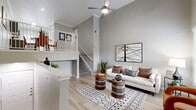 This thoughtfully designed residence makes a striking first impression with its dramatic double-height ceilings in the living area, which flood the space with an airy, open ambiance. Light wood-tone flooring runs throughout the main living spaces, complementing the soft gray walls and crisp crown molding. The expansive living room is anchored by a ceiling fan overhead and features a staircase with white-painted railings leading to an upper loft or landing area, adding architectural character and vertical interest.

The kitchen is both functional and stylish, outfitted with gray shaker-style cabinetry, white quartz countertops, a classic subway tile backsplash, and a full suite of stainless steel appliances. Light wood flooring continues here, and a window above the sink allows natural light to brighten the workspace. A separate exterior door provides added convenience.

The primary bedroom is generously proportioned with plush carpeting, a ceiling fan, and a large window that invites natural light. A second bedroom offers equally comfortable accommodations with soft carpet and ample wall space. The full bathroom is clean and modern, featuring a soaking tub and shower combination with large-format white tile, gray cabinetry, and white countertops — a cohesive and polished finish throughout.