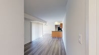 This single-floor unit offers four bedrooms, one bathroom, and a thoughtfully organized layout that maximizes its footprint. The open-concept kitchen and living area serves as the heart of the home, featuring warm honey-toned wood cabinetry, dark granite-style countertops, a peninsula breakfast bar, and a full suite of black appliances including a gas range, dishwasher, and refrigerator. The living room extends naturally from the kitchen and is finished with wood-style plank flooring, neutral white walls, and a sliding glass door dressed in vertical blinds that allows natural light to filter in.

The four bedrooms are accessible via connecting hallways that flow throughout the unit. The generously sized primary bedroom offers ample space, while the remaining bedrooms are finished with plush carpet. Two closets provide dedicated storage, including one with a louvered bifold door and built-in hanging rods and shelving. Additional smaller storage rooms with wood-style flooring offer flexible utility space.

The bathroom is finished with large-format beige wall tiles surrounding a full soaking tub with an overhead shower. Throughout the unit, clean white walls and consistent flooring choices create a cohesive, neutral aesthetic well-suited for a variety of living arrangements.
