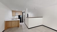 Located at 2440 NE 68th St in Gladstone, Missouri, this efficiently designed single-floor unit makes thoughtful use of its compact footprint. The open living area welcomes you with large-format light gray tile flooring, crisp white walls, black baseboards, and a textured ceiling that runs throughout the space. A bold black entry door pairs with a window fitted with blinds, allowing natural light to fill the room, while a wall-mounted PTAC unit provides climate control.

The kitchen is outfitted with light wood cabinetry, open shelving, a white countertop with an integrated cooktop, and black appliances including a refrigerator. A peninsula with a warm wood-tone surface and built-in lower cabinetry extends into the living area, creating a natural partition that defines each zone without closing off the open layout. Recessed lighting adds a modern touch overhead.

The hallway connects the main living space to the bathroom, which features a white vanity with sink, a toilet, and a glass-enclosed walk-in shower finished with marble-look tile surround and hexagonal mosaic floor tile. Matte black hardware and towel bars add a contemporary, coordinated accent throughout the bathroom. The overall design is clean, modern, and functional.