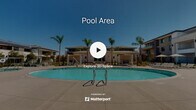 Located at 25150 Jefferson Ave in Murrieta, California, this outdoor amenity space showcases a resort-inspired design tailored for relaxation and recreation under the Southern California sun. The centerpiece is a generously sized, kidney-shaped swimming pool with crystal-clear blue water, complemented by a separate spa for unwinding. Surrounding the pool, a broad concrete deck provides ample space for lounge chairs and seating, ideal for sunbathing or socializing. Multiple pergola-style shade structures with clean, modern lines are positioned throughout the area, offering sheltered spots with patio furniture and market umbrellas. The space is framed by tall, elegant palm trees that enhance the resort atmosphere and provide a sense of privacy. A secure black iron gate with stone accent pillars marks the entrance, reflecting a well-maintained and gated community environment. The multi-story residential buildings surrounding the courtyard feature a contemporary architectural style with neutral stucco exteriors, balconies, and dark-trimmed windows. Thoughtfully placed landscaping with manicured shrubs and ground cover ties the entire outdoor space together, creating a cohesive and inviting community amenity area perfectly suited to the warm Murrieta climate.