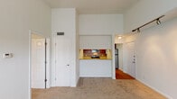 This single-floor unit offers a thoughtfully designed layout with notable architectural details throughout. The living area immediately impresses with soaring ceilings that create a sense of openness and volume. A tile-surround fireplace with a classic white mantel serves as the room's focal point, flanked by a large window that allows generous natural light and outdoor views. Track lighting adds a modern accent to the space, while plush carpet underfoot provides warmth and comfort.

The kitchen is seamlessly integrated into the living space via a pass-through design, making it both functional and visually connected. Rich, warm-toned cabinetry extends to the upper walls, complemented by light granite countertops and a neutral tile backsplash. Stainless steel appliances, including a refrigerator, electric range, and over-the-range microwave, complete the well-equipped space. Hardwood flooring in the kitchen area contrasts nicely with the carpeted living and bedroom areas.

The bedroom is generously sized, featuring a ceiling fan with light fixture, soft carpet, and a window overlooking greenery. The bathroom includes a full soaking tub with a tiled shower surround and chrome fixtures, offering a clean, functional design. Overall, the space presents a comfortable, well-balanced interior.