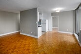 Located at 1 Deauville in Toronto's Don Mills area, this two-bedroom, one-bathroom unit offers a practical and well-organized layout across a single floor. Parquet hardwood flooring flows consistently throughout the living areas and bedrooms, lending warmth to the neutral grey-toned interior.

The living room is a standout feature, characterized by a wide wall of floor-to-ceiling windows and sliding glass door access to a balcony, framing expansive city views. A baseboard heating unit runs beneath the windows, ensuring comfort year-round. The space receives generous natural light throughout the day.

The kitchen is galley-style, featuring white cabinetry, dark countertops, tile flooring, and white appliances including a refrigerator and stove. It connects directly to the entry hallway, creating an efficient flow through the unit.

Both bedrooms continue the parquet flooring and are finished in soft neutral tones. Each benefits from large windows with city views and individual heating units. The primary bedroom offers a comfortable amount of space for furnishing.

The bathroom includes a full tiled tub-shower surround, tile flooring, and standard fixtures. A dedicated laundry room with tile flooring provides added convenience within the unit.
