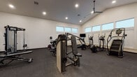 Located at 1440 North Locust Grove Road in Meridian, Idaho, this fitness center offers a generously sized, single-floor workout facility designed to support a comprehensive exercise experience. The space is defined by its striking vaulted ceilings, which lend an open and airy atmosphere, enhanced by recessed lighting and a ceiling fan that help maintain a comfortable environment during workouts. Large windows positioned along the walls allow natural light to flood the interior, contributing to an inviting and energizing ambiance.

The flooring throughout is durable rubber gym matting, providing safety and support across the entire workout area. The facility is well-stocked with a wide selection of professional-grade equipment. Strength training is well represented with multiple selectorized cable and weight machines, a multi-functional cable station, a dumbbell rack with a full range of free weights, and stability balls for functional fitness. Cardio options are equally robust, including elliptical trainers, a stair climber, stationary cycles, and a rowing machine.

A large wall-mounted mirror expands the visual depth of the space while allowing users to monitor their form during exercise. The clean, white walls and neutral palette keep the space feeling modern and focused. This fitness center provides a professional and fully equipped environment well-suited for a broad range of fitness goals.