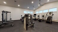 Located at 1440 North Locust Grove Road in Meridian, Idaho, this fitness center offers a generously sized, single-floor workout facility designed to support a comprehensive exercise experience. The space is defined by its striking vaulted ceilings, which lend an open and airy atmosphere, enhanced by recessed lighting and a ceiling fan that help maintain a comfortable environment during workouts. Large windows positioned along the walls allow natural light to flood the interior, contributing to an inviting and energizing ambiance.

The flooring throughout is durable rubber gym matting, providing safety and support across the entire workout area. The facility is well-stocked with a wide selection of professional-grade equipment. Strength training is well represented with multiple selectorized cable and weight machines, a multi-functional cable station, a dumbbell rack with a full range of free weights, and stability balls for functional fitness. Cardio options are equally robust, including elliptical trainers, a stair climber, stationary cycles, and a rowing machine.

A large wall-mounted mirror expands the visual depth of the space while allowing users to monitor their form during exercise. The clean, white walls and neutral palette keep the space feeling modern and focused. This fitness center provides a professional and fully equipped environment well-suited for a broad range of fitness goals.