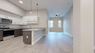 This single-floor unit presents a contemporary design with a cohesive neutral color palette of soft grays and whites throughout. The open-concept layout seamlessly connects the kitchen and living area, creating a spacious, airy feel enhanced by light wood-look flooring. The kitchen is well-appointed with crisp white upper cabinetry, contrasting dark wood-tone lower cabinets, granite countertops, and a peninsula that doubles as a breakfast bar. Stainless steel appliances, including a refrigerator, range, microwave, and dishwasher, complete the functional cooking space. Pendant lighting above the peninsula adds a modern accent. The living area benefits from natural light provided by a pair of windows and is equipped with a ceiling fan overhead.

Multiple bedrooms feature plush carpeting, ample natural light from individual windows, and dedicated closet space. At least one bedroom includes a walk-in style closet with built-in racking. The bathroom is finished with tile flooring, a granite-topped vanity with dark wood cabinetry, and a full tub-shower combination. Throughout the unit, tall ceilings, clean white baseboards, and a consistent modern aesthetic contribute to a bright and well-designed living environment.
