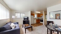 Located at 13803 SE 18th St in Vancouver, WA, this single-floor unit offers a practical and well-appointed layout designed for comfortable everyday living. The open-concept living and dining area flows seamlessly into the kitchen, creating a connected and sociable space. The living room is carpeted and bathed in natural light from multiple windows fitted with vertical blinds, offering views of the surrounding greenery. The kitchen features warm honey-toned wood cabinetry, wood-look flooring, and a full suite of appliances including a refrigerator, electric range, dishwasher, and an under-cabinet range hood — providing ample functionality for home cooking. The primary bedroom is a bright, restful retreat with plush carpeting and a large sliding glass door that opens to a view of lush outdoor landscaping, allowing for generous natural light. A second bedroom offers a quieter, cozier atmosphere with soft carpet and warm ambient lighting. The bathroom is finished with wood-look flooring, a warm wood vanity with under-sink storage, a large mirror, and a shower-tub combination. Throughout the unit, the consistent use of wood-tone accents and neutral wall colors creates a cohesive, inviting ambiance well-suited for a range of residents.