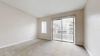 Located at 2600 Oakwood Dr in Bedford, TX, this single-floor, one-bedroom, two-bathroom unit offers a practical and efficiently organized layout. The living area features plush carpeted flooring, neutral beige walls, and a textured ceiling. A large sliding glass door with vertical blinds fills the space with natural light and provides a view of the surrounding exterior, complemented by an additional side window. The bedroom is a comfortable size, also carpeted, with a window dressed in vertical blinds that allows for adjustable light control. The kitchen is equipped with white cabinetry, granite-style countertops, a stainless steel sink, and white appliances including a refrigerator, stove, and microwave. Light wood-look tile flooring in the kitchen adds a clean, modern contrast to the carpeted areas. A hallway connects the main living spaces, with light wood-look flooring continuing through the transitional areas. The bathrooms include a full tub-shower combo with white subway tile surround, a white vanity, and tile flooring, presenting a clean and functional design. Overall, the unit offers a neutral, move-in-ready aesthetic throughout.