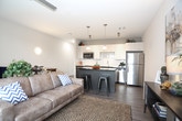 This well-appointed single-floor residence showcases a thoughtfully designed layout that balances modern aesthetics with everyday functionality. The kitchen is a standout feature, offering dark granite countertops that contrast beautifully against crisp white upper cabinetry and rich dark lower cabinets. Stainless steel appliances, including a refrigerator, built-in microwave, and electric range, provide a sleek, professional finish, while a tiled subway backsplash adds a clean, contemporary touch. A central island with pendant lighting and bar seating extends the kitchen into an open-concept dining and living area, making it ideal for entertaining. The living room is bright and welcoming, with large sliding glass doors dressed in vertical blinds that allow generous natural light and outdoor views. Ceiling fans are present throughout, enhancing comfort in each room. The two bedrooms are finished with plush carpeting, ceiling fans, and ample closet space, offering a calm and restful atmosphere. Warm neutral tones carry throughout the unit, lending a cohesive and relaxing ambiance. The bathroom is clean and straightforward, featuring a shower-tub combination. Light wood-tone flooring in the main living areas ties the overall design together with a modern yet inviting character.