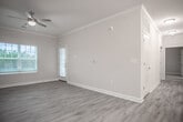Located on Scots Pine Run in North Chesterfield, Virginia, this single-floor residence offers a well-designed, open layout with a clean, contemporary aesthetic throughout. The living area is spacious and bright, featuring light-toned vinyl plank flooring, crown molding, a ceiling fan, and large windows with blinds that allow ample natural light to fill the room. A door provides direct outdoor access, enhancing the sense of openness. The kitchen is thoughtfully appointed with rich dark-stained cabinetry, granite-look countertops, and black and stainless steel appliances including a range, microwave, and refrigerator. The galley-style layout maximizes functionality while maintaining a polished look. The bedrooms are carpeted for comfort and each include ceiling fans. One bedroom features a window with outdoor views, while another includes access to a spacious walk-in closet outfitted with wire shelving for organized storage. The bathroom includes a full tub and shower combination with clean white surround tile, brushed nickel fixtures, and a vanity with matching dark cabinetry. A dedicated laundry nook with washer/dryer hookups adds everyday convenience. Light neutral tones, white trim, and consistent finishes create a cohesive and welcoming atmosphere throughout the entire space.