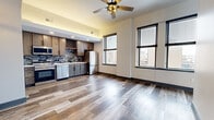 This efficiently designed 1-bedroom, 1-bathroom unit offers a thoughtful single-floor layout that maximizes every square foot. Wide-plank wood-look flooring runs seamlessly throughout, lending a cohesive and contemporary aesthetic to the entire space.

The open-concept living area is bathed in natural light from large windows fitted with blinds, offering urban views of the surrounding cityscape. A ceiling fan anchors the living space, adding both style and function.

The kitchen is a standout feature, equipped with a full suite of stainless steel appliances including a range, over-the-range microwave, dishwasher, and French door refrigerator. Rich wood cabinetry, a built-in wine rack, and a striking mosaic tile backsplash complete the polished look, with ample counter space and recessed lighting overhead.

The bedroom is a comfortable retreat, featuring multiple windows with urban views and a stylish sliding barn door that opens to a dedicated closet. The bathroom is well-finished, showcasing a subway-tiled tub and shower surround, matte black fixtures, a floating-style vanity, and wood-look flooring. A separate laundry area with a stacked washer and dryer adds everyday convenience.