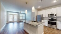 This thoughtfully designed 2-bedroom, 2-bathroom residence features a single-floor open-concept layout that seamlessly connects the kitchen, dining, and living areas. The kitchen is a standout centerpiece, showcasing white shaker cabinetry, granite countertops, a subway-tile backsplash, and a large island with an undermount sink and pendant lighting overhead. Stainless steel appliances — including a refrigerator, electric range, and over-the-range microwave — complete the space. Wood-style flooring flows throughout the main living areas, adding warmth and continuity. The living area benefits from natural light via large windows and is topped with a ceiling fan. Both bathrooms are finished with granite countertops and white cabinetry; the primary bath features a dual-sink vanity with a framed mirror, while the secondary bath offers a tiled tub-shower combination. The bedrooms are carpeted and include ceiling fans and generous closet space, with at least one walk-in closet with built-in shelving and rods. A dedicated laundry area with washer and dryer is tucked behind panel doors, adding everyday convenience to this clean and modern home.