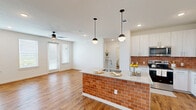 Located at 1000 E Yager Ln in Austin, TX, this single-story, 3-bedroom, 2-bathroom home offers a clean, modern design with thoughtful finishes throughout. Warm wood-look flooring flows seamlessly across the entire floor plan, creating a cohesive and inviting atmosphere.

The open-concept living room is bright and airy, featuring recessed lighting, a ceiling fan, and multiple windows with blinds that invite natural light while maintaining privacy. The space connects fluidly to the kitchen, which serves as a standout centerpiece of the home. The kitchen boasts a striking island wrapped in terracotta brick-style tile, topped with granite countertops and pendant globe lights. White shaker-style cabinetry extends to the ceiling, complemented by a matching brick-tile backsplash and stainless steel appliances, including a refrigerator, range, and microwave. Built-in open shelving near the kitchen adds both function and character.

The three bedrooms are comfortably sized, each featuring wood-look flooring, recessed lighting, and windows with natural views. One bedroom includes a ceiling fan and built-in wall shelving. The bathrooms are finished with granite vanity countertops, white tile tub surrounds, and wood-look flooring. Panel-style interior doors and neutral wall tones complete the home's clean, contemporary aesthetic.