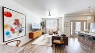 This 1-bedroom, 1-bathroom residence offers a smartly designed open-concept layout that maximizes every square foot. The combined kitchen and living area serves as the heart of the home, where warm wood-tone cabinetry, white subway tile backsplash, stainless steel appliances, and a large kitchen island with a waterfall countertop and bar seating create an inviting and functional space. Pendant lighting adds a modern flair above the island. The living area features light wood-style flooring, a ceiling fan, and large windows that fill the room with natural light, while a built-in workspace nook offers a dedicated area for productivity. The bedroom is carpeted and generously proportioned, with windows on multiple walls providing ample daylight and a comfortable, restful atmosphere. The bathroom showcases a sleek walnut-finish vanity, white quartz countertop, a large mirror with contemporary lighting, and wood-look flooring. The spacious closet includes full-width hanging storage and conveniently houses an in-unit stacked washer and dryer. Throughout the residence, a cohesive mid-century modern aesthetic ties together warm wood tones, clean white walls, and stylish finishes for a polished, livable feel.