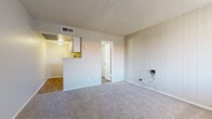 This single-floor unit offers a straightforward, functional layout designed for comfortable everyday living. The main living area is finished with neutral-toned carpet and smooth, light-colored walls accented by vertical paneling detail, creating a clean and understated aesthetic. A textured ceiling adds a classic touch throughout the space. A pass-through opening connects the living area to the kitchen, offering a sense of openness between the two spaces.

The galley-style kitchen is efficiently designed, featuring white upper and lower cabinetry, a light speckled countertop, a stainless steel sink, a coil-burner range, and a full-size refrigerator. Warm hardwood-style flooring runs through the kitchen, adding contrast to the lighter tones of the cabinetry and walls. Overhead ventilation keeps the space practical and well-equipped.

The bathroom includes a vanity with a single basin sink, speckled countertop, white cabinetry below, a large mirror, and hardwood-style flooring that continues from the kitchen. The bedroom is a well-proportioned room with plush carpeting, neutral walls, a textured ceiling, and a window that allows natural light to filter in. A paneled exterior door provides direct outside access from the bedroom, adding a unique functional element to the space.