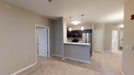 This single-floor residence is designed with an open-concept layout that seamlessly connects the kitchen and living area, creating a spacious and functional environment. The kitchen is outfitted with dark espresso cabinetry that contrasts neatly against light countertops and a white peninsula that serves as both a workspace and a visual divider between the two areas. Stainless steel appliances, including a refrigerator, stove, and microwave, add a modern, polished finish. Two pendant lights hang above the kitchen, providing focused task lighting while contributing to the overall aesthetic. The living area features neutral beige carpeting that complements the warm greige wall tones, fostering a calm and cohesive atmosphere throughout. Arched panel doors lead to additional rooms, lending a classic architectural touch that softens the otherwise contemporary design. The open sightlines between rooms enhance the sense of spaciousness, making the layout feel welcoming and easy to navigate. Overall, the space presents a clean, move-in-ready aesthetic with a balanced blend of modern fixtures and timeless architectural details.