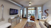 This single-floor residence offers a thoughtfully designed layout that balances comfort and functionality. The kitchen is a standout feature, outfitted with stainless steel appliances including a French door refrigerator, electric range, and built-in microwave. Warm maple cabinetry pairs with dark granite countertops and a bold checkered tile backsplash, while a curved breakfast bar with pendant lighting overhead creates an inviting space for casual dining. The living area is bright and welcoming, with light hardwood flooring, exposed ductwork that adds an industrial character, and large glass doors that open directly to a private patio, filling the room with natural light and outdoor views. The bedroom is carpeted for comfort and features generous natural light from sheer-curtained windows, with direct access to additional spaces. The full bathroom is well-appointed, featuring a soaking tub with a tiled surround, a single-sink vanity with dark stone countertops, and a large mirror that amplifies the sense of space. Throughout the residence, neutral tones and consistent finishes create a cohesive aesthetic, while the overall layout promotes a smooth and practical flow between living, cooking, and private spaces.