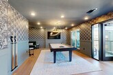Located at 3305 South Blvd in Charlotte, NC, this well-appointed amenity lounge offers a sophisticated and inviting atmosphere across a single floor. The space is defined by its bold, patterned wallpaper, warm hardwood flooring, and a cohesive slate-blue and gold color palette that runs throughout.

The main game room serves as a central gathering area, anchored by a full-size pool table set atop a plush area rug. A striking gold circular chandelier hangs overhead, complemented by recessed lighting, while a wall-mounted flat-screen TV adds an entertainment focal point. A cozy lounge nook features a curved green velvet sectional sofa with wall sconces, ideal for relaxed viewing or socializing.

Adjacent to the game room, a dining and kitchenette area provides a functional yet stylish setting. It includes a round dining table with mixed seating, a built-in wet bar or kitchenette with marble-style backsplash, teal cabinetry, open shelving with greenery, and under-counter appliances. Pendant lighting with dark drum shades adds an elegant touch overhead.

Large black-framed glass doors open directly onto an outdoor balcony, flooding the interior with natural light and offering expansive views of the Charlotte skyline. The balcony provides additional seating, making this space ideal for both casual gatherings and events.