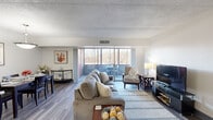 Located at 1100 Penn Center Blvd in Pittsburgh, PA, this single-floor residence offers a well-organized layout designed for comfortable everyday living. The spacious living room is anchored by wood-look flooring and flows directly toward a wall of sliding glass doors, opening onto a private balcony with views of surrounding natural wooded scenery — a standout feature that brings abundant natural light into the space. The living area provides generous room for seating and entertainment arrangements. Adjacent to the living room, a dedicated dining area accommodates a full dining table for four, illuminated by a modern pendant light fixture, and connects seamlessly to the kitchen. The galley-style kitchen features white cabinetry, dark granite-style countertops, full appliances including an electric range and refrigerator, and a convenient pass-through counter with bar seating — ideal for casual meals. The bedroom offers a calm retreat with plush carpeting, a window with blinds, and ample wall space. The bathroom is finished with classic white tile surrounding a full soaking tub and shower combination. Throughout the residence, consistent wood-look flooring in the main areas and neutral wall tones create a clean, cohesive aesthetic.