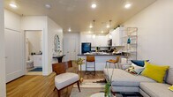 This single-floor residence offers a well-designed, open-concept layout that seamlessly connects the living, dining, and kitchen areas into one cohesive space. Wood-look plank flooring flows throughout the main living area, complementing the warm, neutral color palette. The kitchen is outfitted with white shaker cabinetry extending to the ceiling, dark granite-style countertops, black appliances including a full-size refrigerator and electric range, and a peninsula with bar seating illuminated by pendant lighting. The living area provides comfortable space for lounging and entertaining, with a glass-paneled door allowing natural light to filter in.

The primary bedroom features a horizontal shiplap accent wall, a generous window with blinds, and plush carpeting, creating a calm, restful atmosphere. The second bedroom is a comfortably sized, carpeted room with a window and corner shelving. The bathroom includes white cabinetry with dark countertops, an undermount sink, a large mirror, and a tub/shower combination with tile flooring. A dedicated laundry closet houses a stacked full-size washer and dryer, adding everyday convenience to this thoughtfully arranged home.