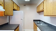 Located in Maplewood, this single-floor residence offers a straightforward and functional layout designed for comfortable everyday living. The galley-style kitchen is efficiently arranged with warm oak cabinetry lining both walls, dark speckled countertops, a double-basin stainless steel sink, and white appliances including a full-size refrigerator and range. Light-toned tile flooring and overhead ventilation keep the space practical and easy to maintain.

The living area features neutral-toned carpet, clean white baseboards, and a front entry door that allows natural light to filter in. A hallway connects the main living space to the rest of the home, which includes multiple carpeted bedrooms finished in soft, neutral tones. One bedroom benefits from a window with blinds that brings in natural light, complemented by a ceiling fan with a built-in light fixture. The additional bedroom is quiet and simply finished, offering a versatile space.

The bathroom includes a full tub-and-shower combination with white tile surround, chrome fixtures, a toilet, and a vanity with a white countertop. Light tile flooring and an overhead vent complete the space. Throughout the residence, the consistent use of neutral tones and practical finishes creates a cohesive and move-in ready environment.